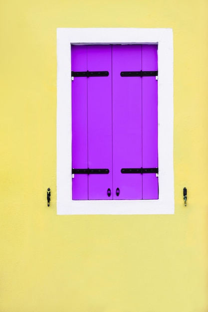 Geel geschilderde gevel van het huis en raam met lavendelluiken