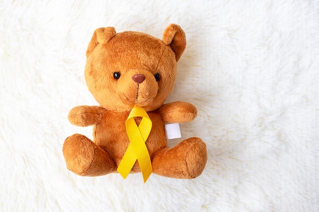 Geel lint met berenpop op witte achtergrond ter ondersteuning van het leven en de ziekte van kinderen. September Childhood Cancer Awareness maand en Wereldkankerdag concept