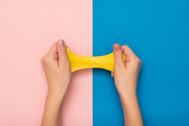 Geel slijm uitgerekt door kinderhanden op een roze en blauwe achtergrond. Speelgoed anti-stressprogramma. Speelgoed voor de ontwikkeling van de handmotoriek.