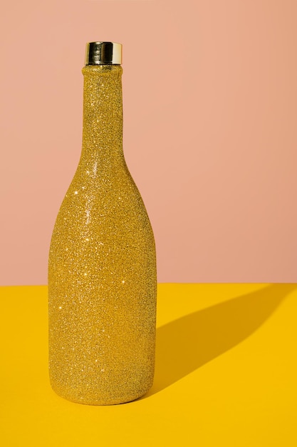 Foto geelgouden glitter champagnefles met scherpe schaduw op gele en roze achtergrond. creatief concept van verjaardagsfeestje viering ontwerp. minimaal abstract kleurrijk en levendig behangidee.