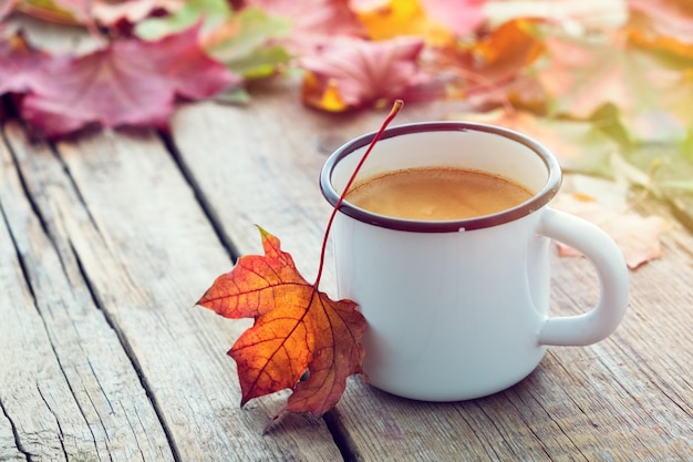 Geëmailleerde kop koffie en gevallen esdoornbladeren op houten bord