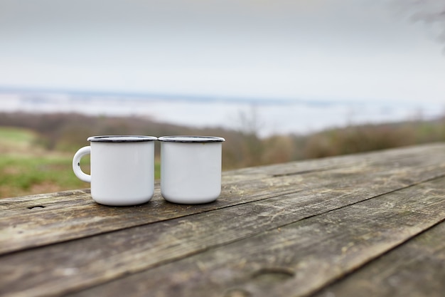 Geëmailleerde twee kopjes thee in de natuur op houten achtergrond, liefde, reisconcept, Lifestyle moment in de natuur, kopieer ruimte.