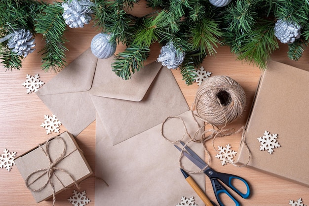 Geen afval kerstconcept. Geschenken in handgemaakte dozen, gerecycled papier, envelop, touw, schaar, kunstmatige vuren takken en houten sneeuwvlokken, bovenaanzicht, plat gelegd. Ecologische kerstcadeaus