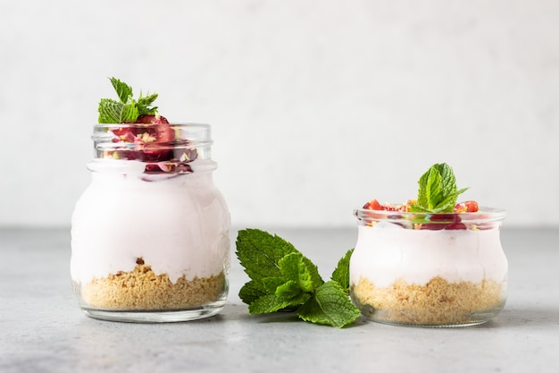 Geen gebakken cheesecake met kers in glazen potten, verse kersen en munt op een grijze steen