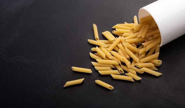 Geen gluten. Gezonde pasta verstrooiing van beker op zwarte achtergrond