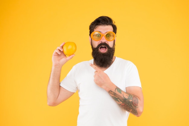 Geen paniek, het is organisch. Bebaarde man wijzende vinger naar biologisch oranje fruit op gele achtergrond. Hipster die natuurlijke biologische voeding kiest. De biologische keuze.