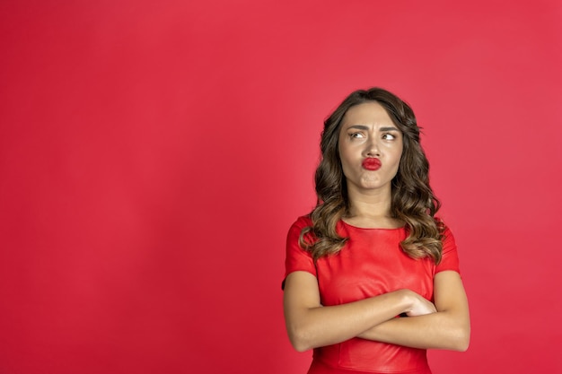 Geërgerd brunette vrouw in rode jurk op een rode achtergrond.