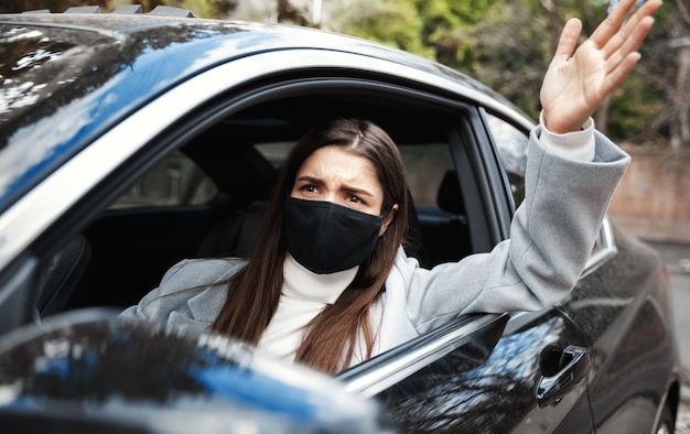 Geërgerd vrouw in gezichtsmasker uitbrander bestuurder, zittend in de auto en kijkt uit raam, ruzie met persoon in auto vooruit