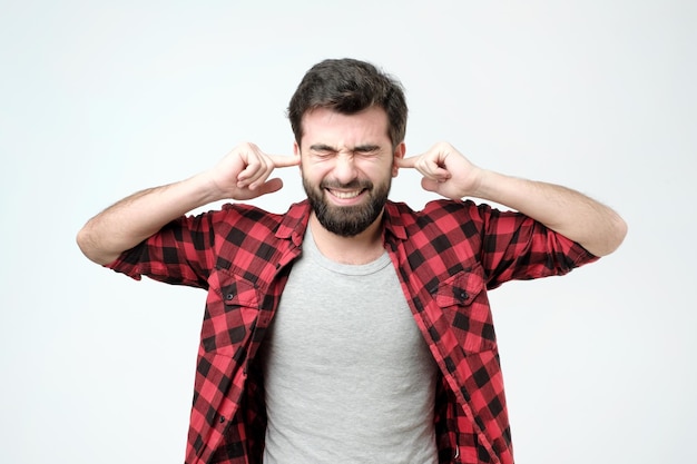 Foto geërgerde jonge man die oren stopt met handen studio shoot