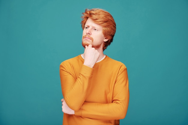 Geërgerde jonge roodharige man met baard die ogen dicht houdt en oren bedekt met handen tegen blauwe muur