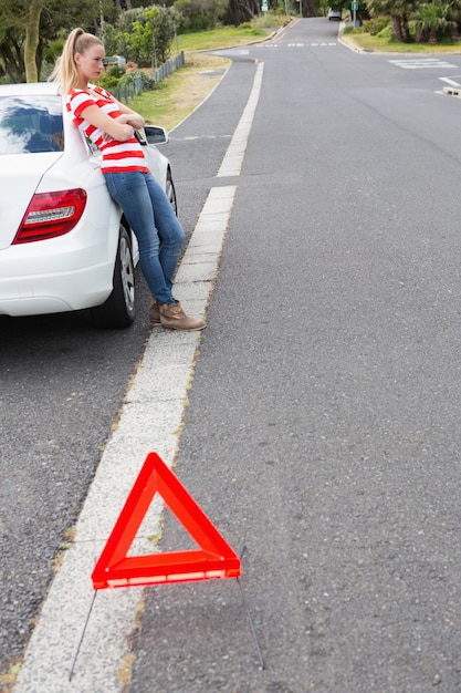 Geërgerde jonge vrouw naast haar opgesplitste auto