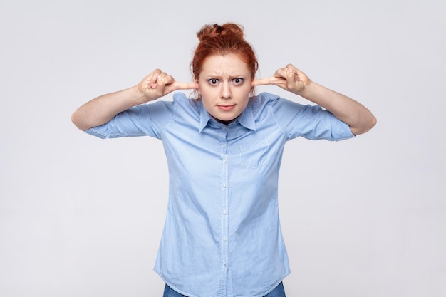 Geërgerde roodharige vrouw met een blauw shirt geïrriteerd door hard geluid dat de oren bedekt en grimassen van de pijn