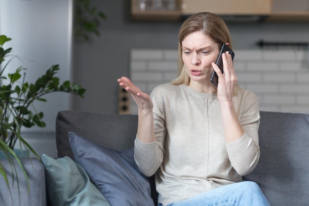 Geërgerde vrouw thuis zittend op de bank en pratend aan de telefoon