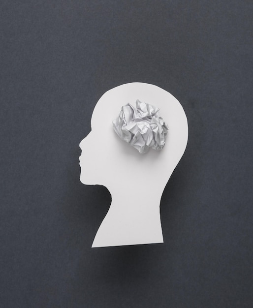 Geestelijke gezondheid hersenziekte dementie verwarde gedachten Papercut silhouet van een menselijk hoofd met een gerimpeld stuk papier op een grijze achtergrond