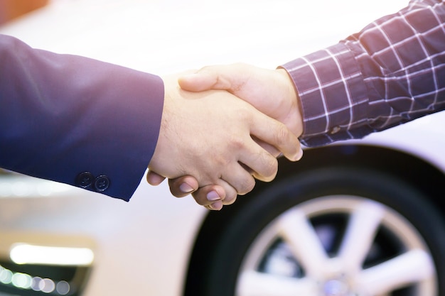 Gefeliciteerd. close-up van jonge zakenman schudden handen met de autodealer in autoshow na een succesvolle deal.