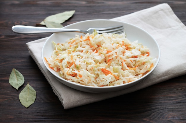 Gefermenteerde kool. Veganistisch eten. Zuurkool met wortel en kruiden in kom op de donkere achtergrond. Trend eten.