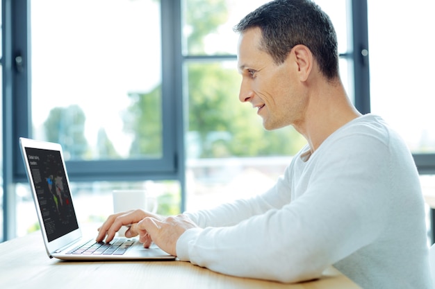 Gefocust zijn. Positieve vrolijke opgetogen man zit achter de laptop en werkt eraan terwijl hij gefocust is op zijn taak