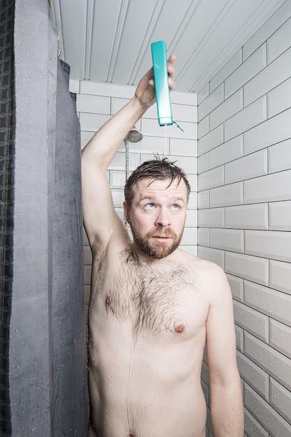 Gefocuste man giet shampoo op zijn hoofd terwijl hij onder de douche staat onder een stroom water
