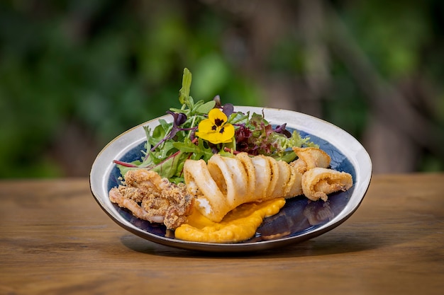 Gefrituurde calamares met groene salade op een houten tafel