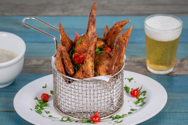 Gefrituurde kippenvleugel geserveerd met saus en een glas bier op blauw hout