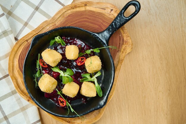 Gefrituurde krokante camembert met cranberrysaus in een decoratieve pan op een houten bord. Close-up, selectieve aandacht