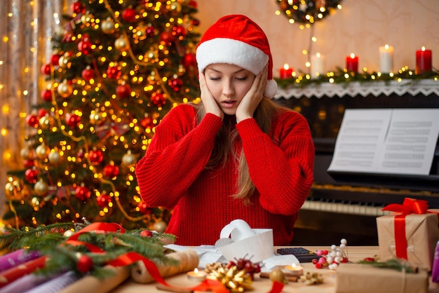 Gefrustreerd jong meisje in rode trui en kerstmuts met gestresste gezichtsuitdrukking