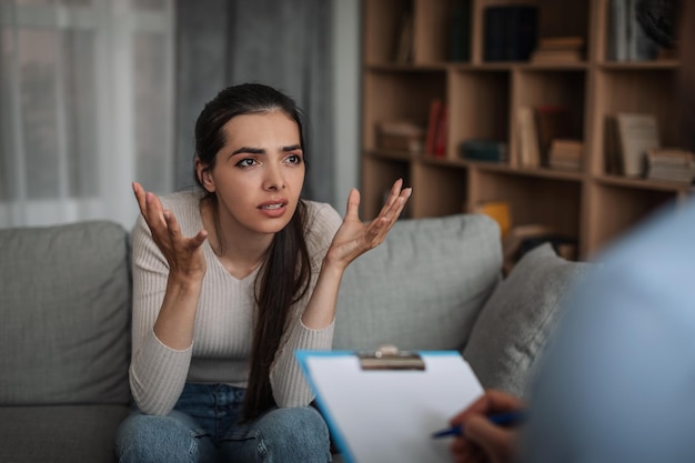 Gefrustreerde emotionele jonge Europese vrouw bij overleg met arts psycholoog met tablet