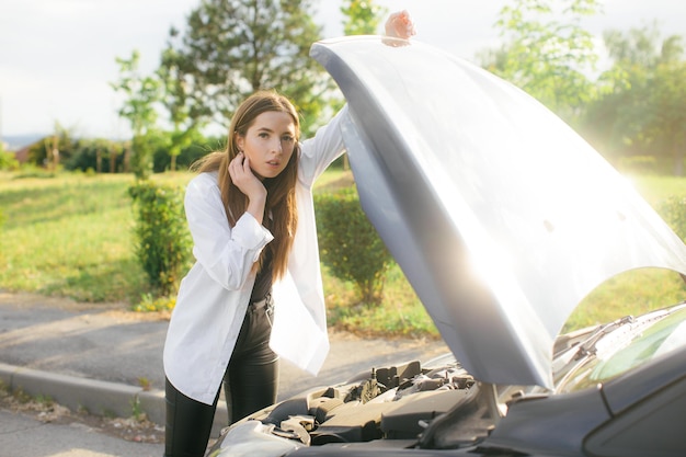 Gefrustreerde jonge vrouw die op straat naar kapotte automotor kijkt