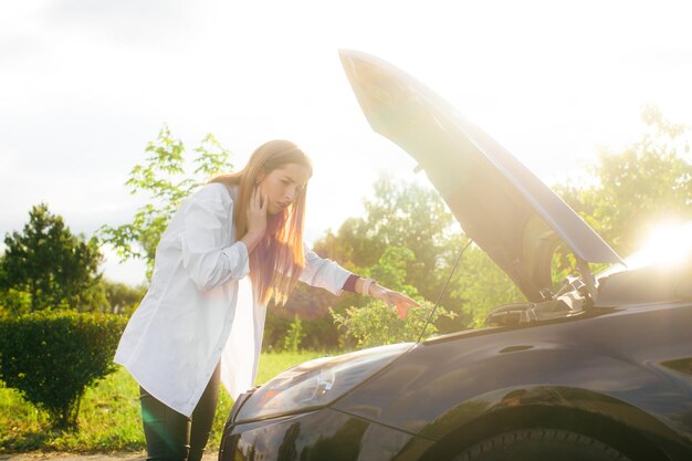 Gefrustreerde jonge vrouw die op straat naar kapotte automotor kijkt