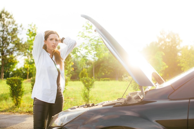 Gefrustreerde jonge vrouw die op straat naar kapotte automotor kijkt