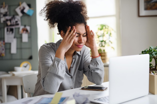 Gefrustreerde jonge vrouw met laptop die binnenshuis werkt, thuiskantoorconcept.