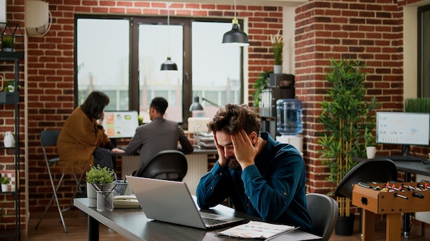 Gefrustreerde overwerkte zakenman die aan gegevensrapport werkt en zich gestrest voelt over de presentatiedeadline. Vermoeide uitgeputte persoon in spanning, laptop gebruikend en in wanhoop zijn, werkwanhoop.