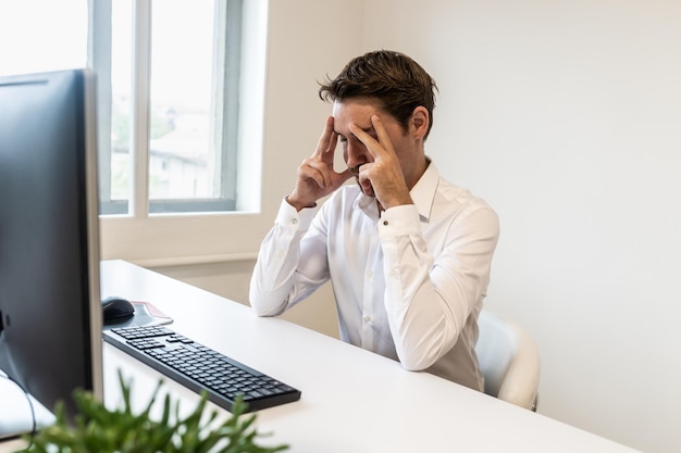 Gefrustreerde zakenman die aan zijn bureau voor de computer zit en zijn hoofd in handen leunt