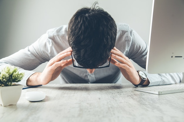 Gefrustreerde zakenman zittend op het bureau met de hand op het hoofd in kantoor