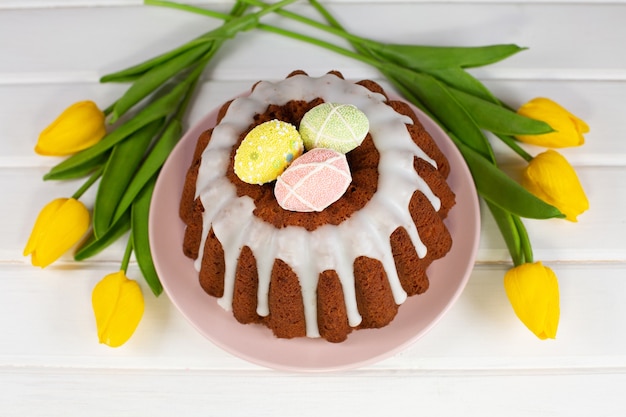 Geglazuurde paascake versierd met mini-eieren, snoep en gele tulpen