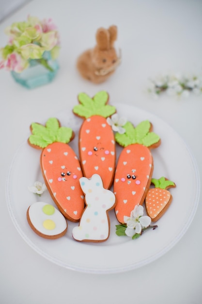 Geglazuurde paaskoekjes en witte lentebloem op een wit bord Wortelkonijntje en eivormige koekjes