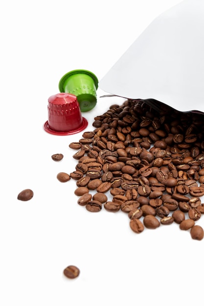 Gegoten gebrande koffiebonen uit de verpakking voor de bereiding van een aromatische drank en veelkleurige capsules geïsoleerd op een witte achtergrond verticale close-up ruimte voor tekst