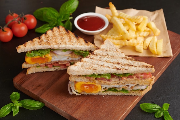 Gegrild en sandwich met spek, gebakken ei, tomaat en sla geserveerd op een houten snijplank
