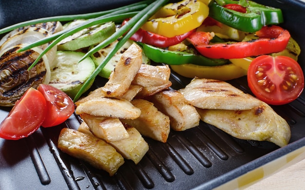 Gegrild kippenvlees op de grill met groenten op de achtergrond.