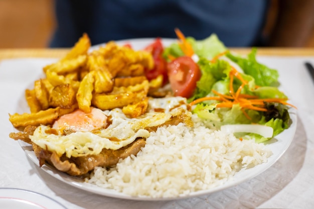 Gegrild vlees met gebakken ei rijst aardappel en salade op witte plaat