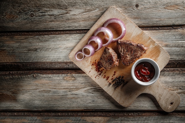 Gegrild vlees met kruiden en tomatensaus op een versleten houten achtergrond