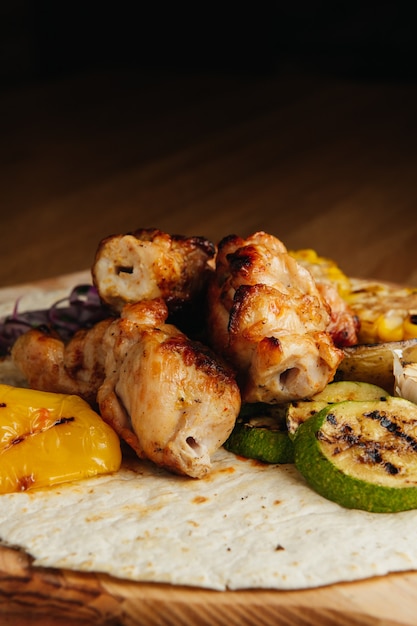 Gegrild vlees op spiesjes, shish kebab met groenten op een houten bord. kip sjasliek.