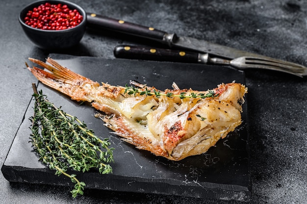 Gegrilde baars van de Rode Zee op een snijplank. Zwarte achtergrond. Bovenaanzicht.