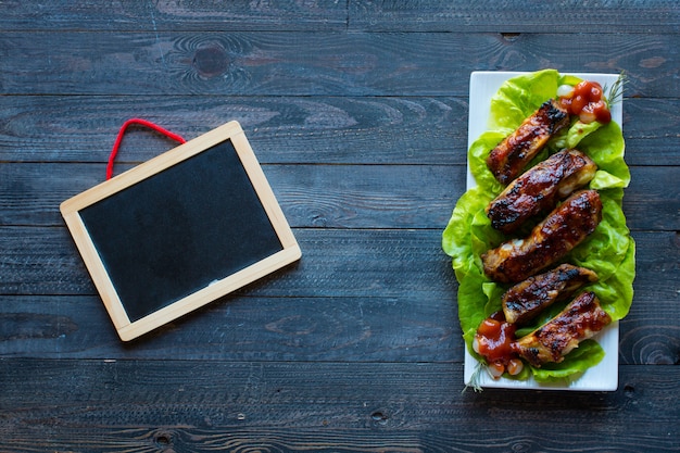 Gegrilde barbecue varkensribbetjes met groenten op een houten achtergrond; vrije ruimte voor tekst.