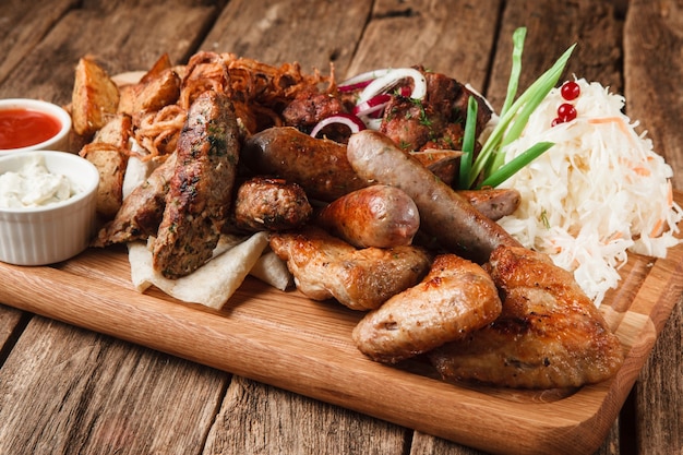 Gegrilde bedoelde en worstjes met smakelijke sauzen, aardappelpartjes en zuurkool geserveerd op rustieke houten tafel.