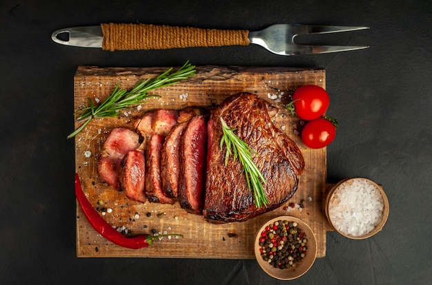 Gegrilde biefstuk, kruiden en specerijen op een snijplank op een stenen achtergrond, bovenaanzicht