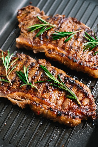 Gegrilde biefstuk met rozemarijn in zwarte grillpan op tafel.