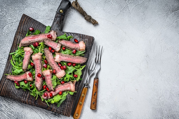 Gegrilde biefstuk met salade van rucola bladeren op rustieke snijplank gesneden