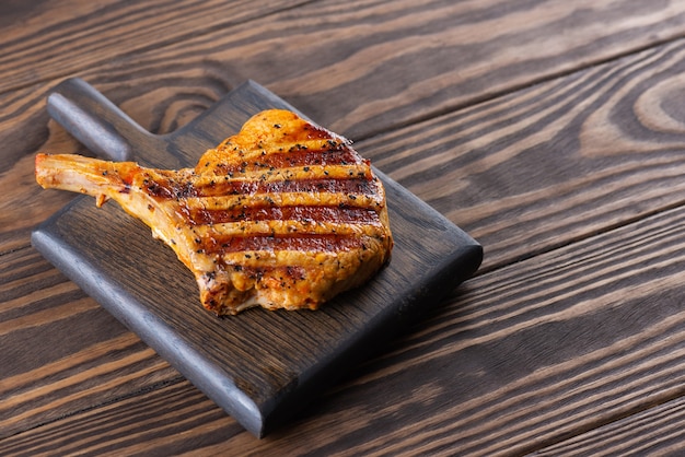 Gegrilde bone steak op een donkere houten plank.