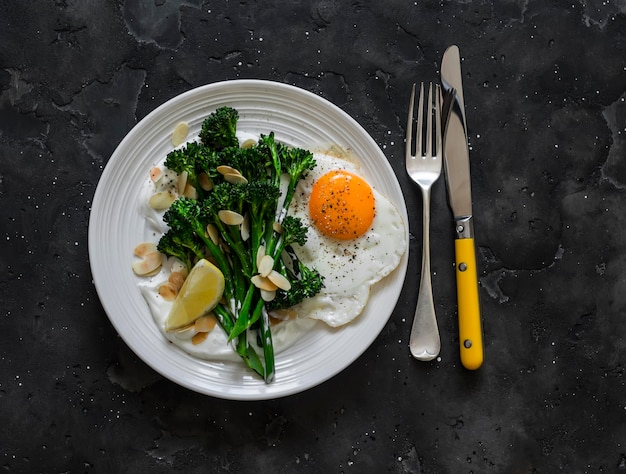 Gegrilde broccolini met Griekse yoghurt en geroosterde amandelen en gebakken ei op een donkere achtergrond Heerlijke ontbijtbrunch